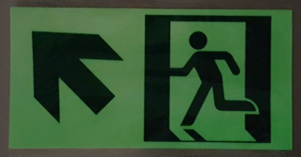 Zielony prostokątny znak z białą strzałką w lewo w hali przemysłowej